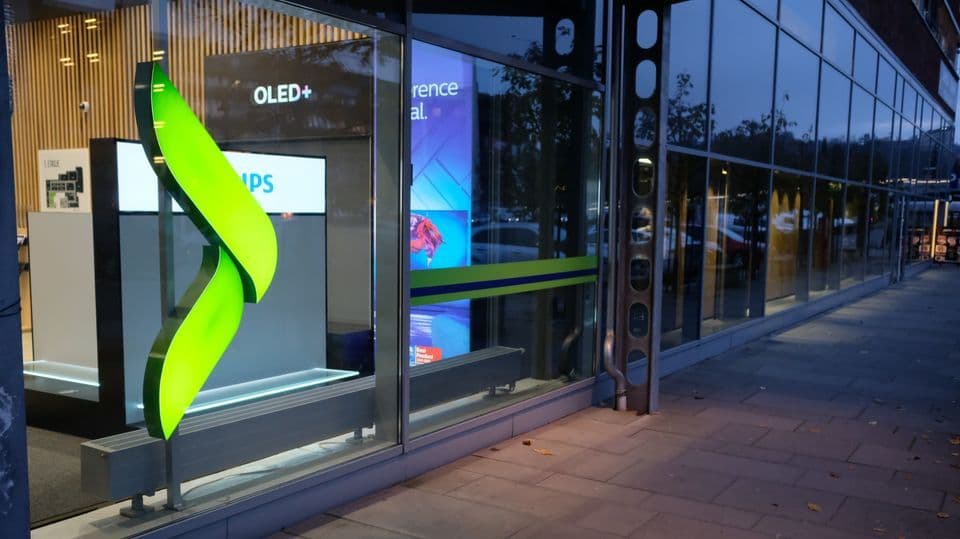 A storefront with a glowing green leaf sculpture, and reflective windows at dusk.
