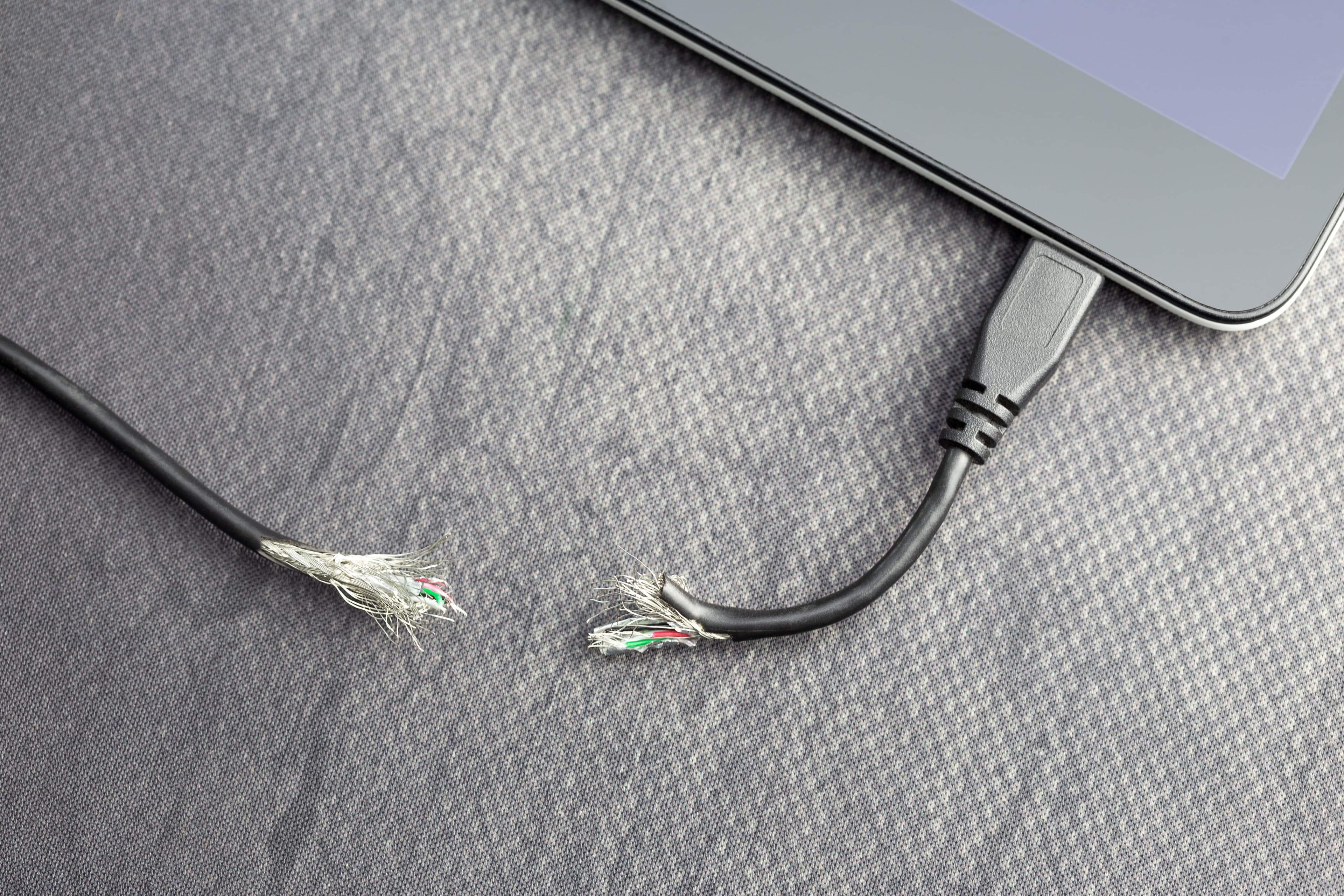 A broken charging cable with frayed wires, one end plugged into a tablet.