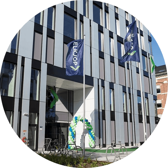 Modern building with "ELKJOP" flags, a blue and green balloon arch, and bicycles outside.