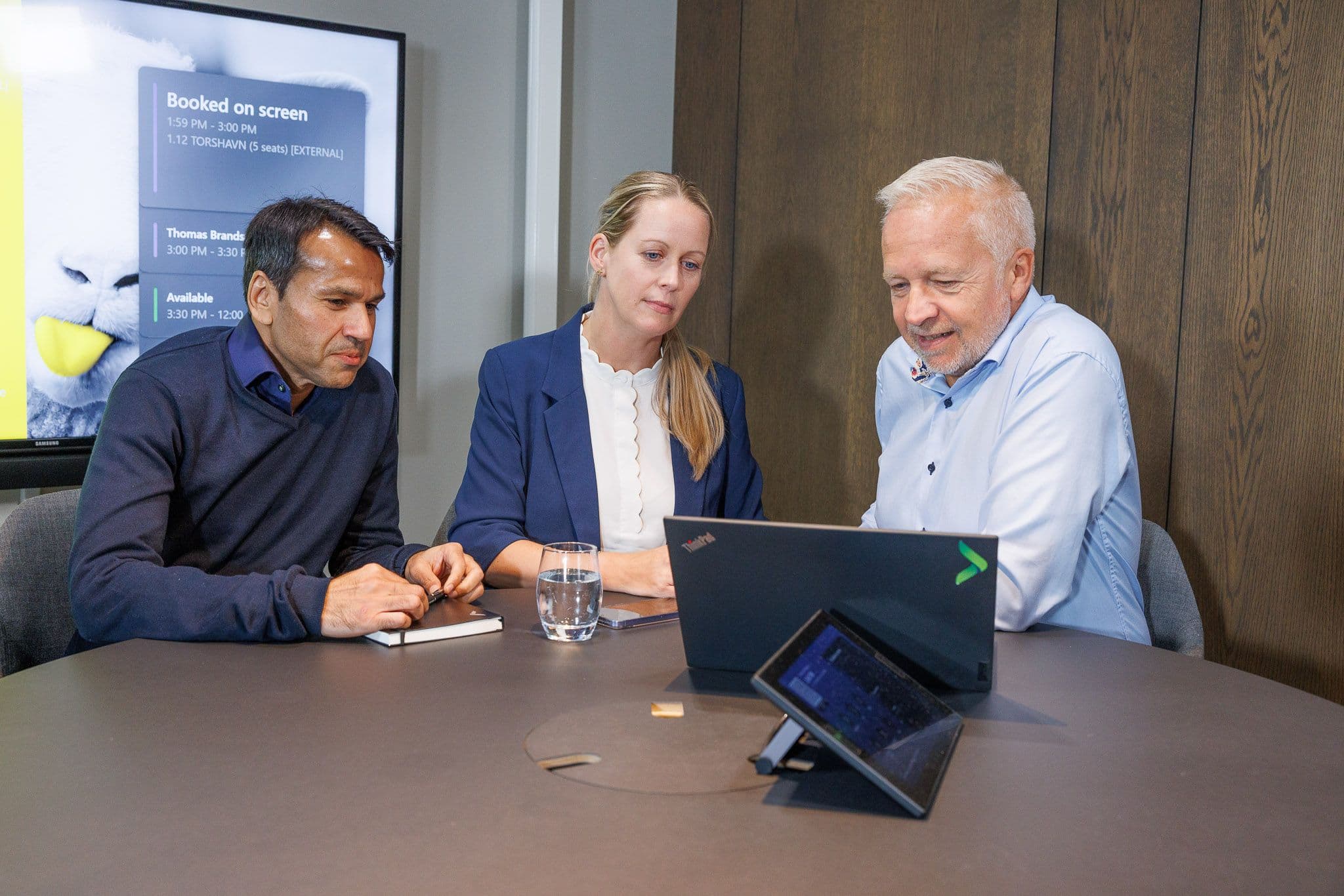 Three business people look at laptops and a tablet during a meeting.