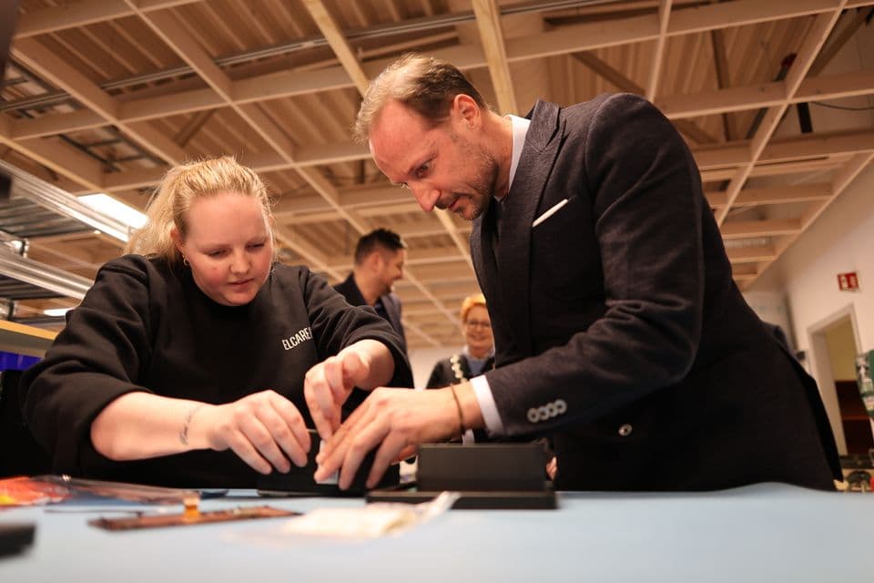 A woman and a man in a suit lean over a table, working on a small electronic device.